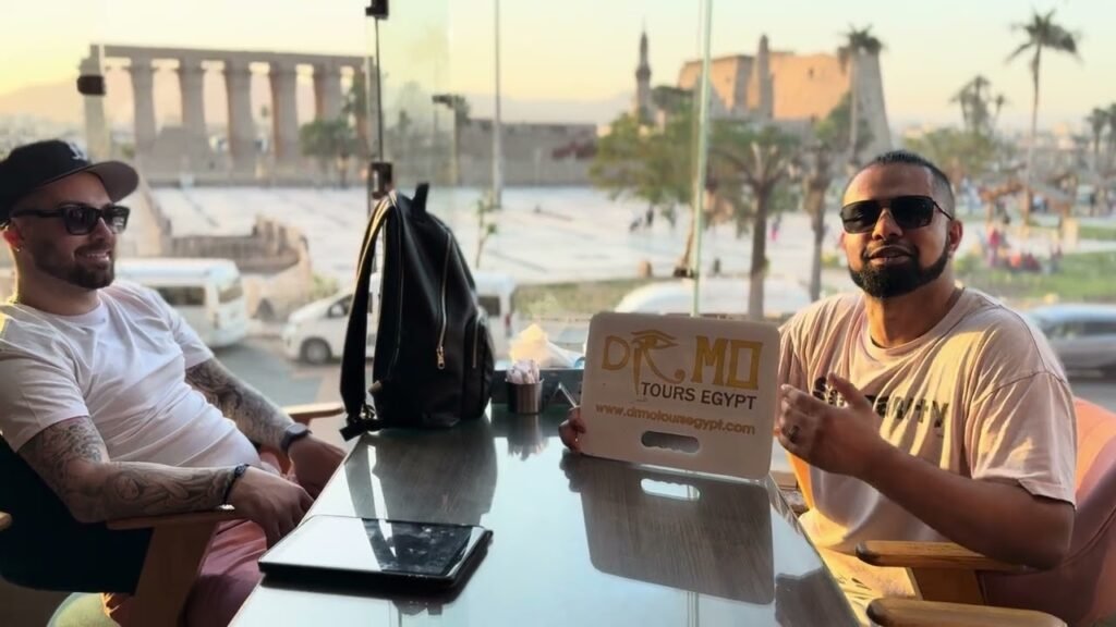 Two guests from Canada at a cafe facing Luxor Temple with a Dr Mo Tours sign